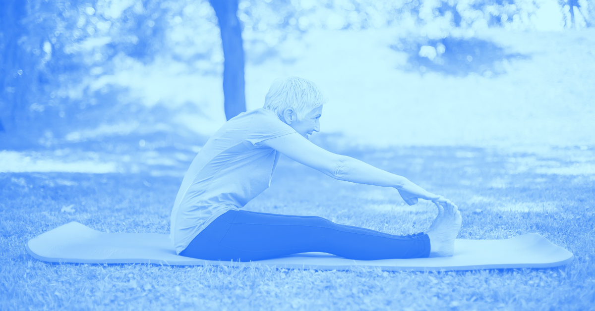 Elderly person touching their toes while on a yoga mat outside