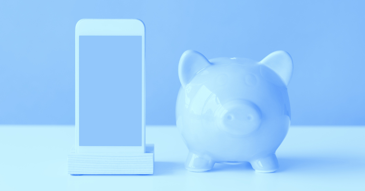 A phone propped up next to a piggy bank.